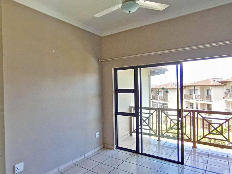 An empty bedroom featuring tiled flooring, a ceiling fan, and a sliding glass door providing access to a private balcony.