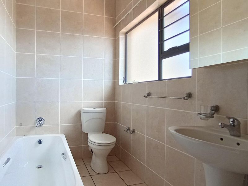 A functional bathroom featuring a bathtub, pedestal basin, and toilet with neutral wall and floor tiling.