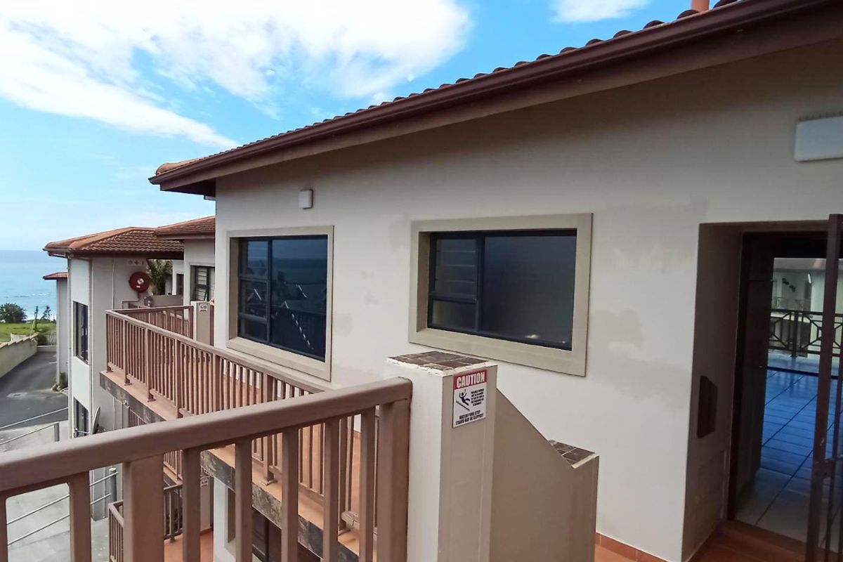 Exterior view of an apartment balcony featuring metal balustrades, aluminium windows, and a tiled roof with coastal views in the background.