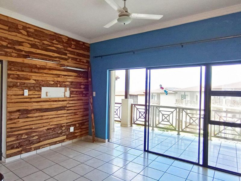 An empty living room featuring tiled floors, a ceiling fan, and a sliding door leading to a balcony, with a unique timber-clad feature wall.