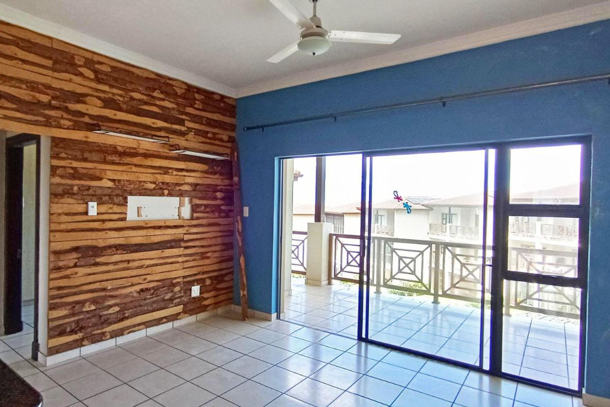 An empty living room featuring tiled floors, a ceiling fan, and a sliding door leading to a balcony, with a unique timber-clad feature wall.