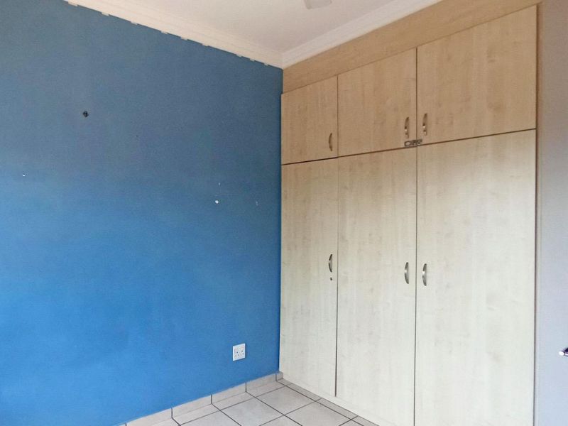 A bedroom featuring built-in cupboards, tiled flooring, and a blue accent wall, offering a functional space ready for personalization.