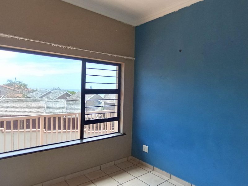 An empty bedroom featuring tiled flooring, security bars on the window, and a blue accent wall.