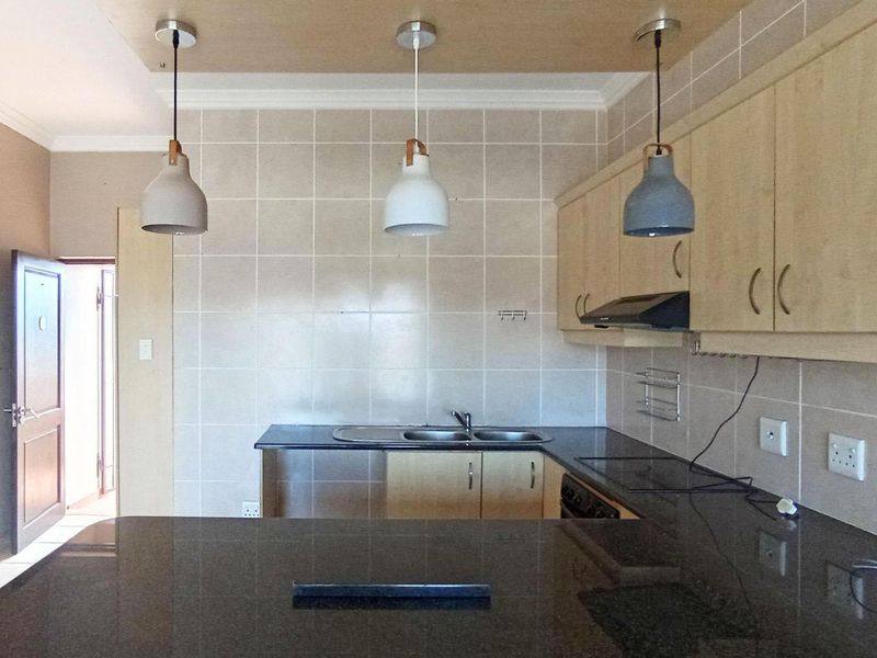 A functional kitchen featuring light wood cabinetry, dark granite countertops, a double basin sink, and a tiled backsplash with modern pendant lighting.