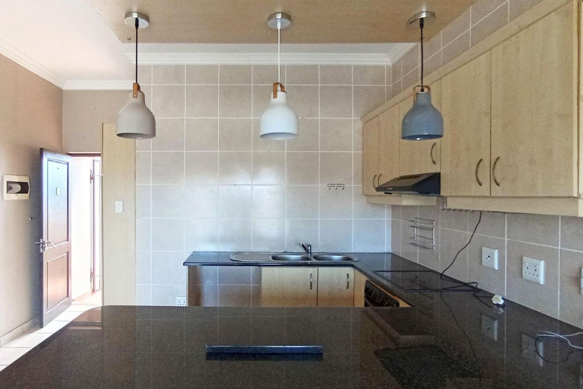 A functional kitchen featuring light wood cabinetry, dark granite countertops, a double basin sink, and a tiled backsplash with modern pendant lighting.