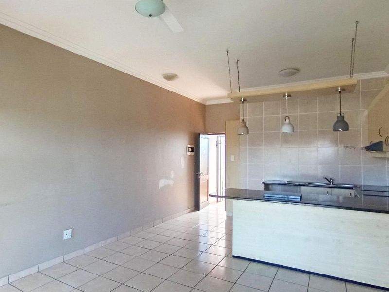 Open-plan living area featuring tiled floors, a kitchen with granite countertops, pendant lighting, and direct access to an exterior entrance.
