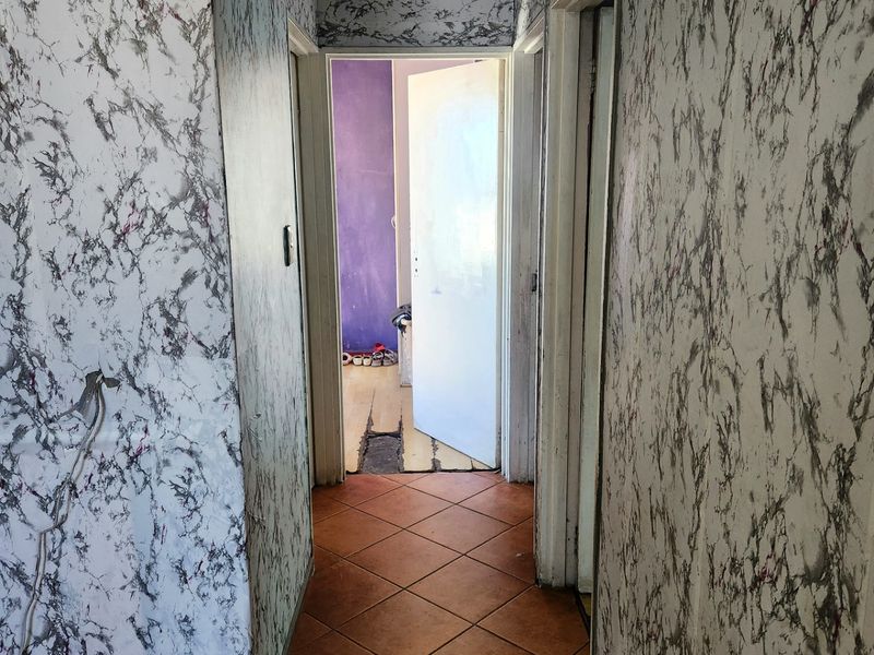 A narrow hallway featuring tiled flooring and dated marble-effect wallpaper, leading to an adjacent room with visible flooring wear.