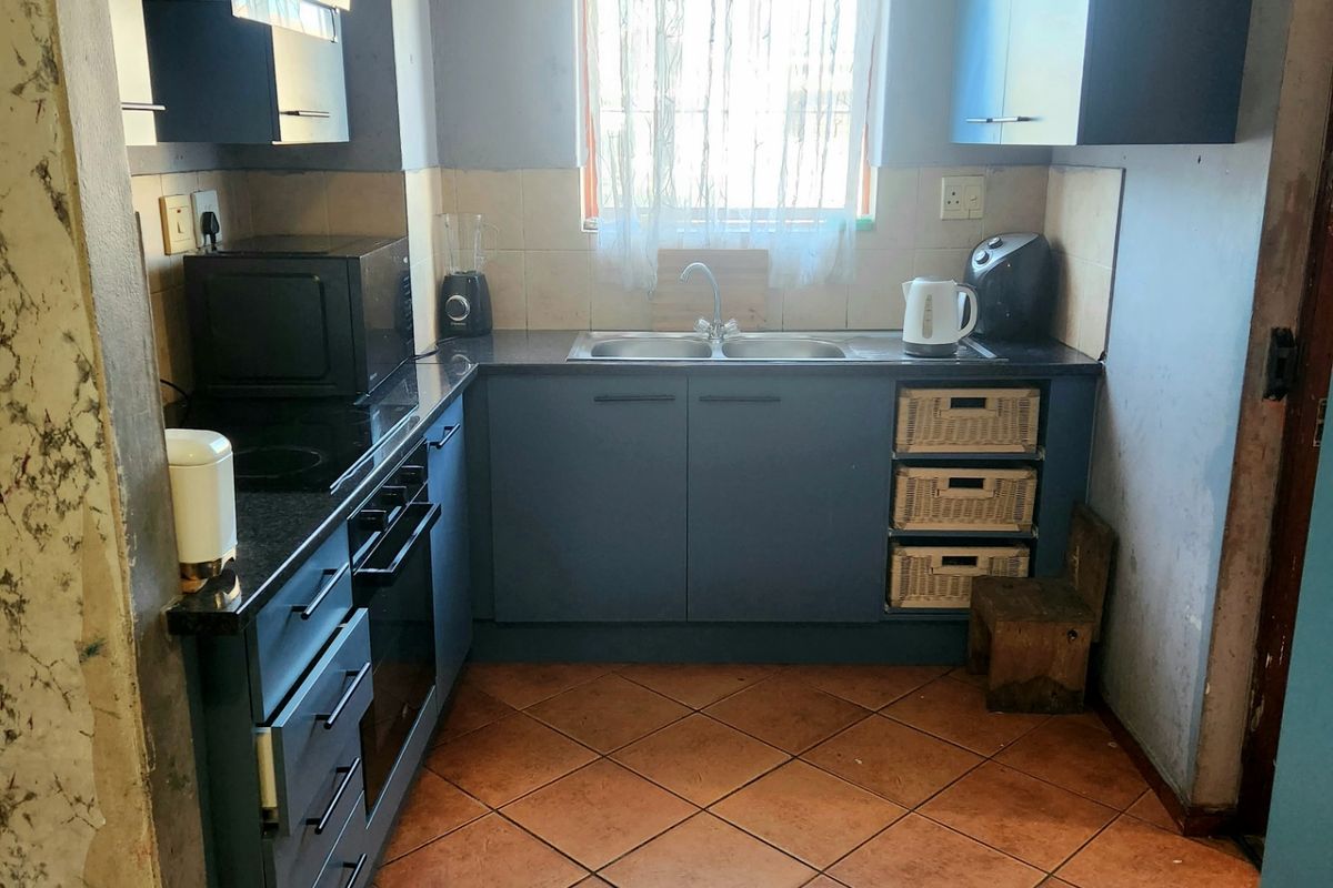 Compact kitchen featuring blue cabinetry, built-in oven and hob, double sink, and tiled flooring. Requires cosmetic updates to wall finishes.