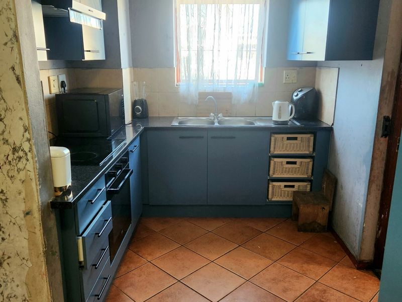 Compact kitchen featuring blue cabinetry, built-in oven and hob, double sink, and tiled flooring. Requires cosmetic updates to wall finishes.