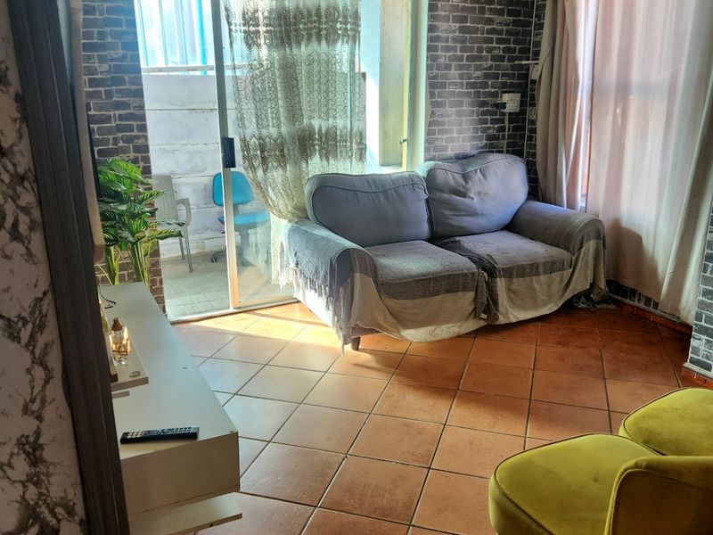A living room featuring ceramic floor tiles, brick-effect wall cladding, and a sliding glass door providing access to an outdoor area.