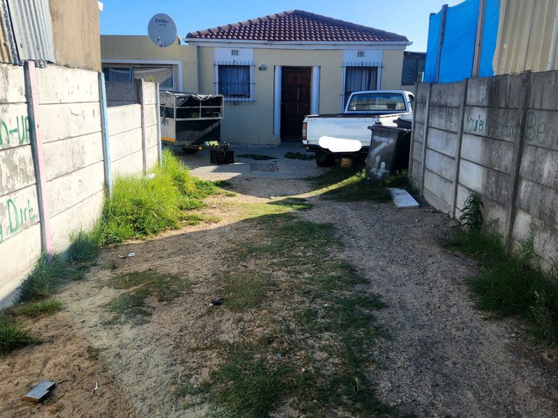 Front view of a detached house featuring a tiled roof, security bars, and a large unpaved driveway area enclosed by precast concrete boundary walls.