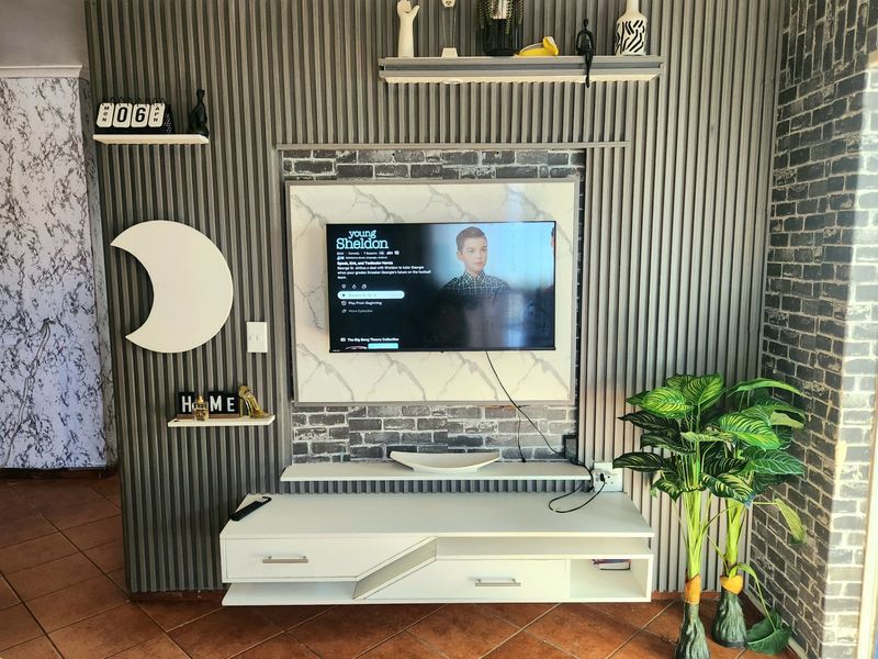 A living room featuring a custom media wall with slatted paneling, faux brick accents, a marble-effect TV mount, and a floating console unit.