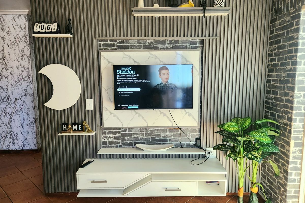 A living room featuring a custom media wall with slatted paneling, faux brick accents, a marble-effect TV mount, and a floating console unit.