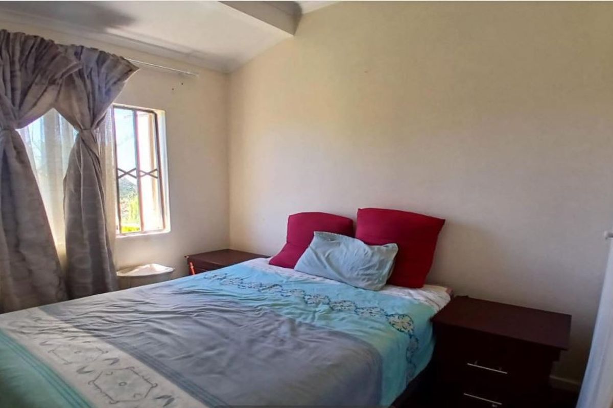 A standard bedroom featuring a window with security bars, providing natural light and basic functional space.