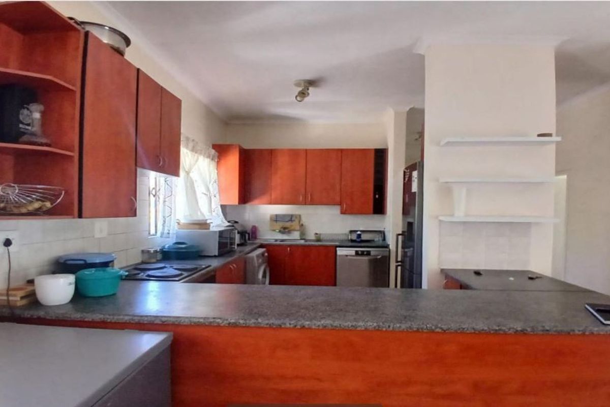 A functional kitchen featuring wood-tone cabinetry, stone-look countertops, a tiled backsplash, and open shelving, offering a practical layout for daily meal preparation.
