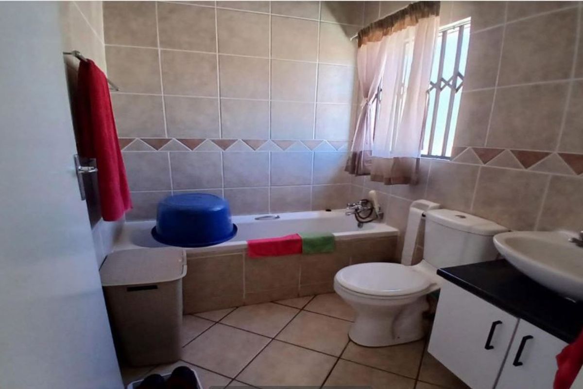 A functional bathroom featuring a bathtub, toilet, and vanity cabinet with a washbasin, finished with neutral wall and floor tiles.