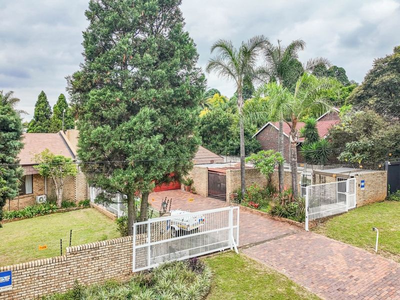 Elevated view of a residential property featuring a brick-paved driveway, perimeter brick walling, established garden, and secure gated entrance.