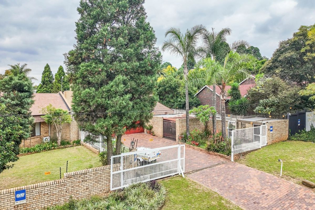 Elevated view of a residential property featuring a brick-paved driveway, perimeter brick walling, established garden, and secure gated entrance.