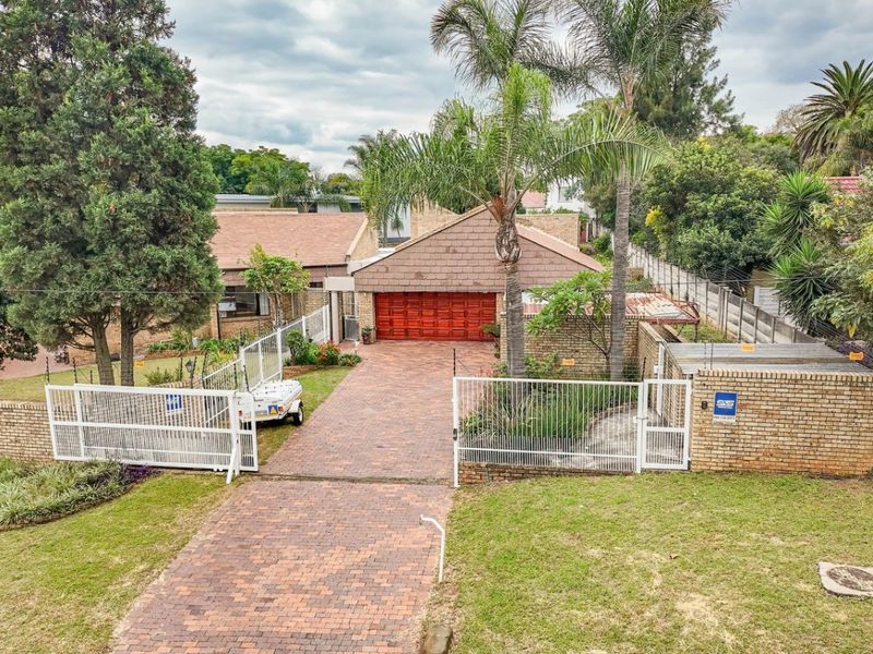 Aerial view of a residential property featuring a brick-paved driveway, double garage, perimeter fencing, and established garden landscaping.