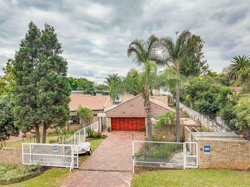 Front exterior view of a single-story brick house featuring a paved driveway, double garage, and established garden with perimeter security fencing.