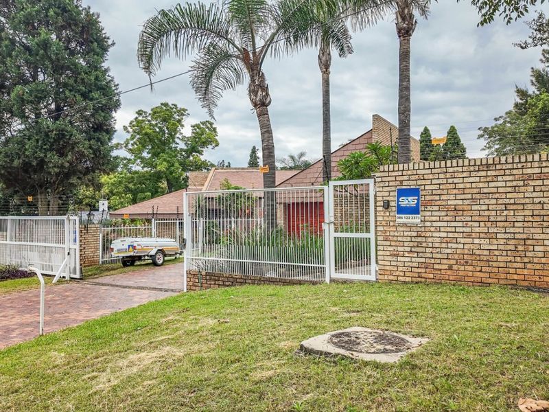 Front exterior view of the property featuring a brick boundary wall, gated entrance, paved driveway, and established garden landscaping.