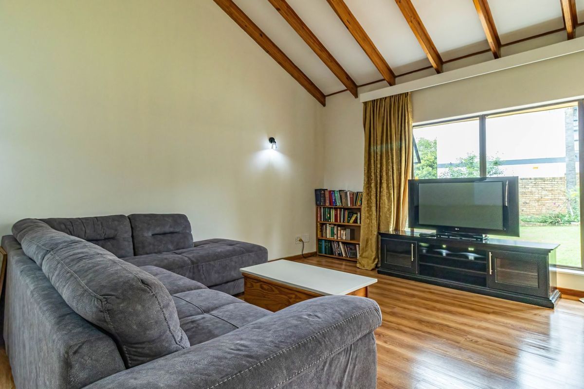 A comfortable living room featuring high vaulted ceilings with exposed timber beams, laminate flooring, and large windows overlooking the garden.