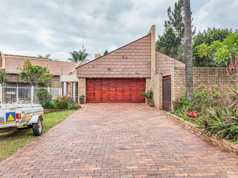Front exterior view of the property featuring a paved driveway, a double garage with wooden doors, and established garden beds.