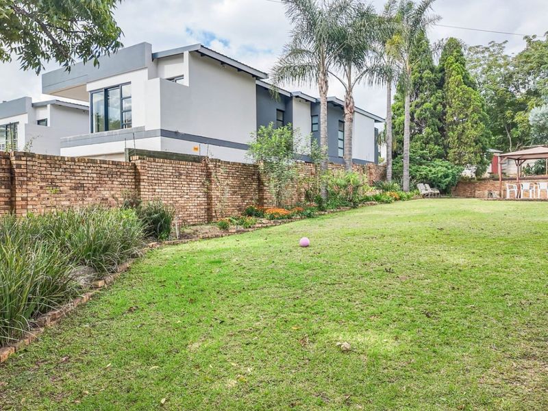 Spacious rear garden featuring a well-maintained lawn, established perimeter brick wall, and a paved patio area with a gazebo.