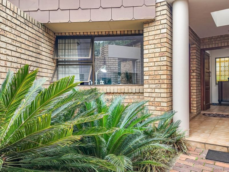 A welcoming front entrance featuring a brick facade, a covered porch area, and established cycad landscaping leading to a solid timber front door.