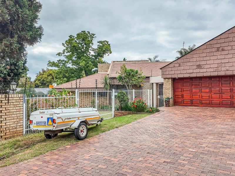 Front exterior view of the house featuring a paved driveway, double wooden garage door, and perimeter fencing with security electric wiring.