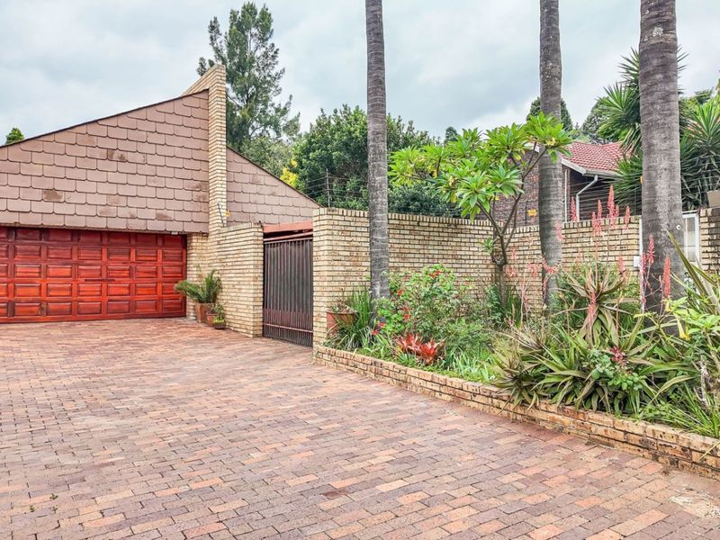 A paved driveway leading to a double garage with a distinctive pitched roof, complemented by a brick boundary wall and established garden beds.