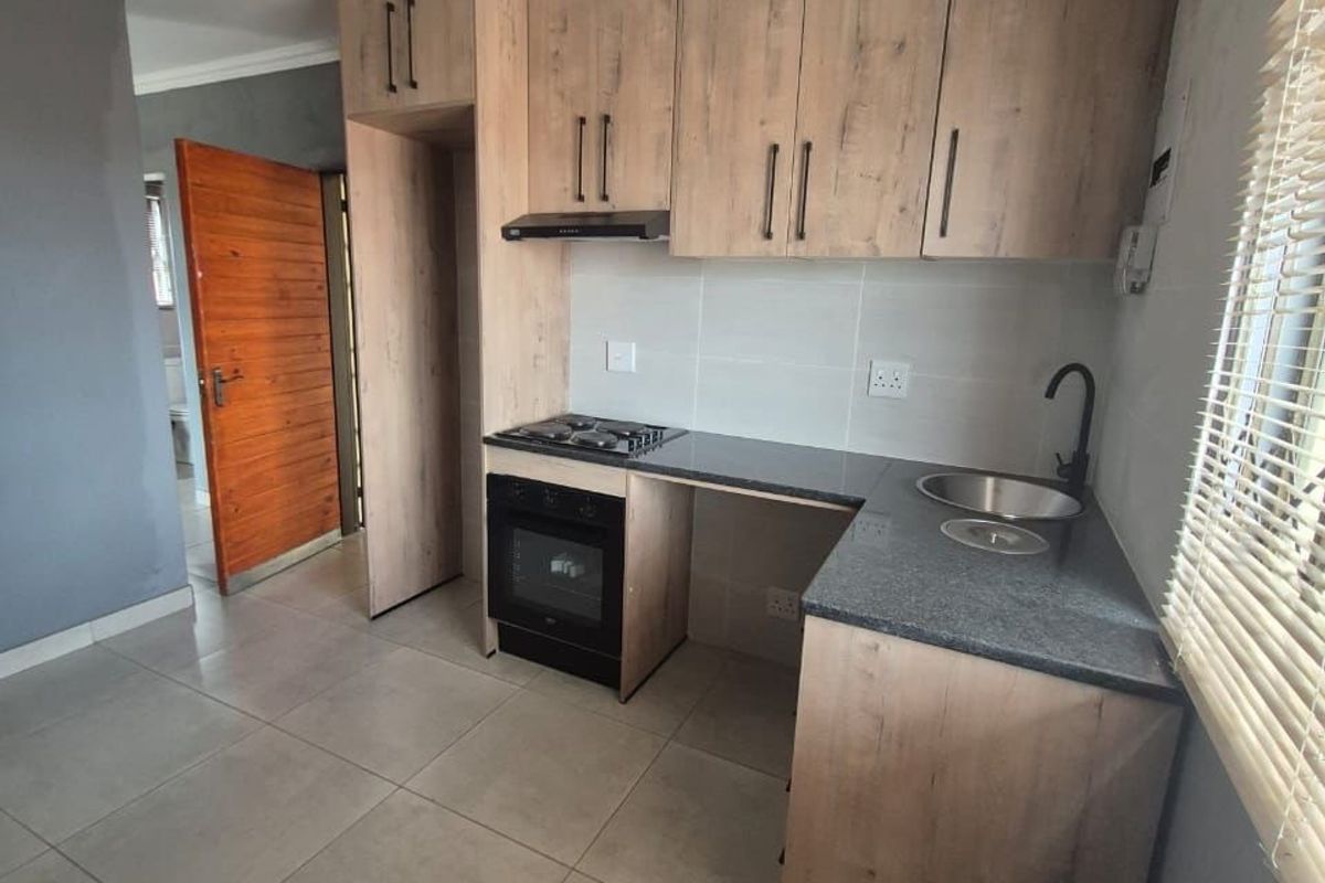 Modern kitchen featuring wood-look cabinetry, stone countertops, built-in oven, gas hob, and tiled flooring in a clean, contemporary layout.