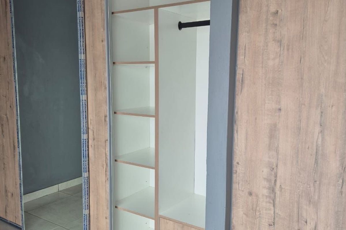 A modern built-in wardrobe featuring wood-grain finish, sliding mirror doors, internal shelving, hanging space, and integrated drawers.