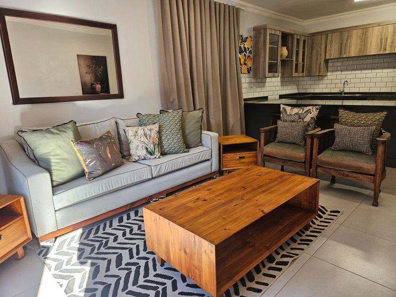 An open-plan living area featuring a modern kitchen with subway tile backsplash, dark countertops, and tiled flooring, seamlessly connected to the lounge space.