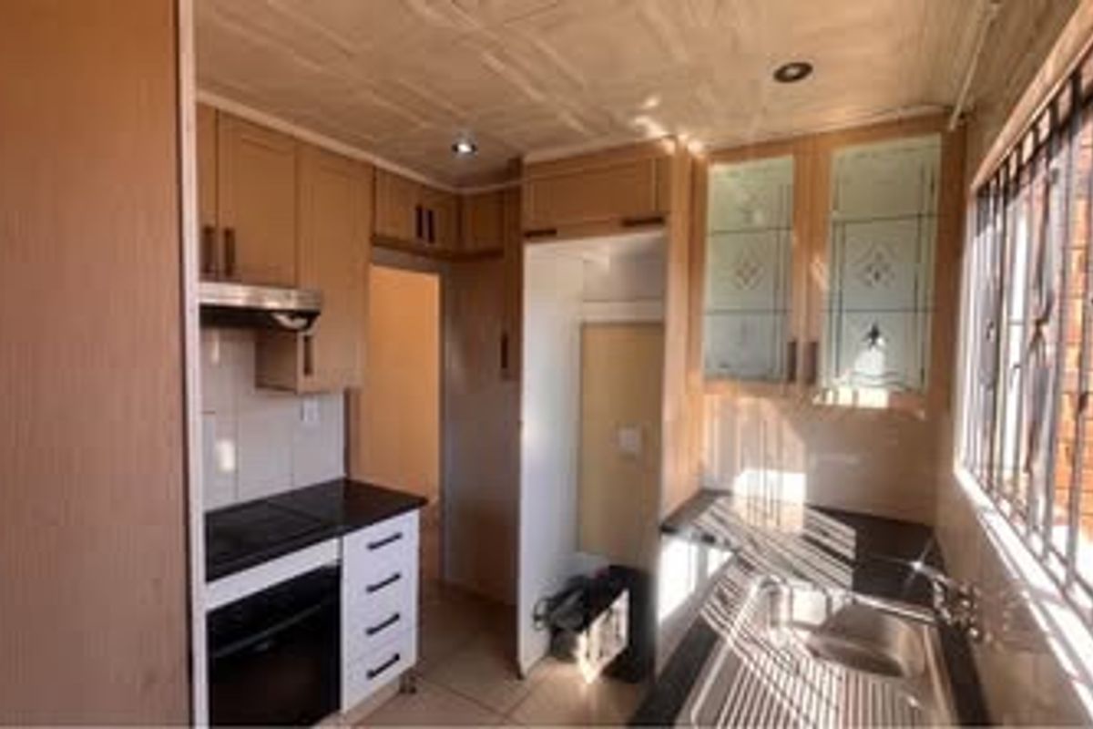 A functional kitchen featuring built-in cabinetry, an integrated oven and hob, stainless steel sink, and security bars on the windows.