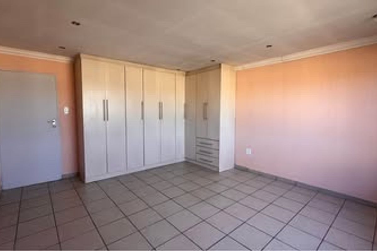 A spacious, empty bedroom featuring neutral tiled flooring, built-in cupboards with ample storage, and recessed ceiling lighting.