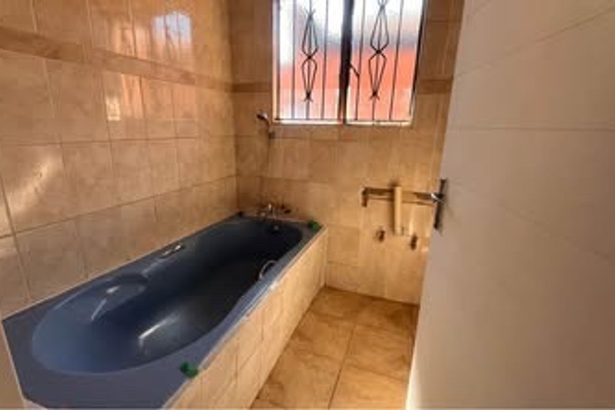 A functional bathroom featuring a built-in bathtub, tiled walls and flooring, and a window with security bars.
