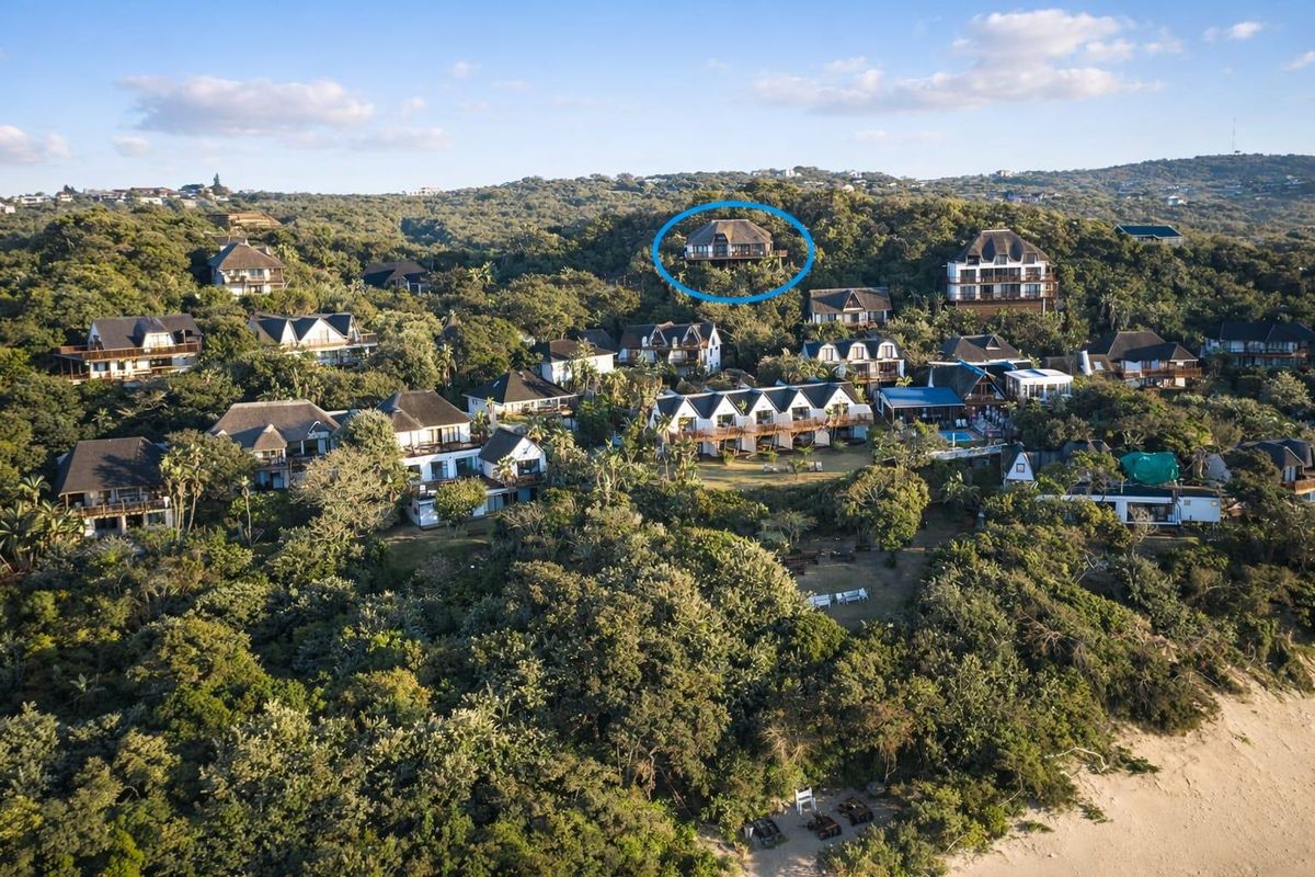 Aerial view of a coastal estate featuring multiple residential properties nestled within dense indigenous forest and natural landscape.