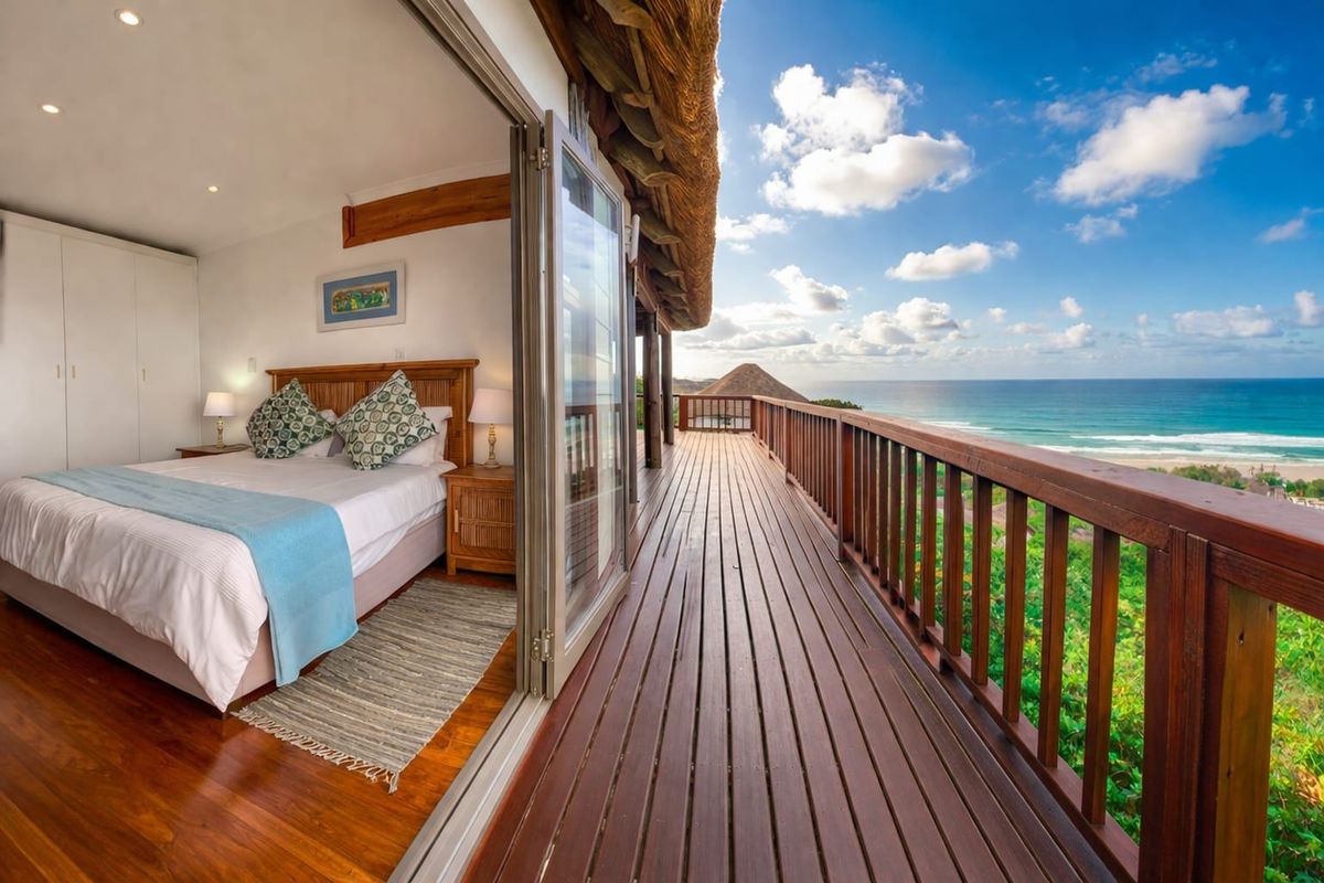 A well-maintained bedroom featuring built-in cupboards and seamless access to a spacious wooden deck with stunning ocean views and a thatched roof.