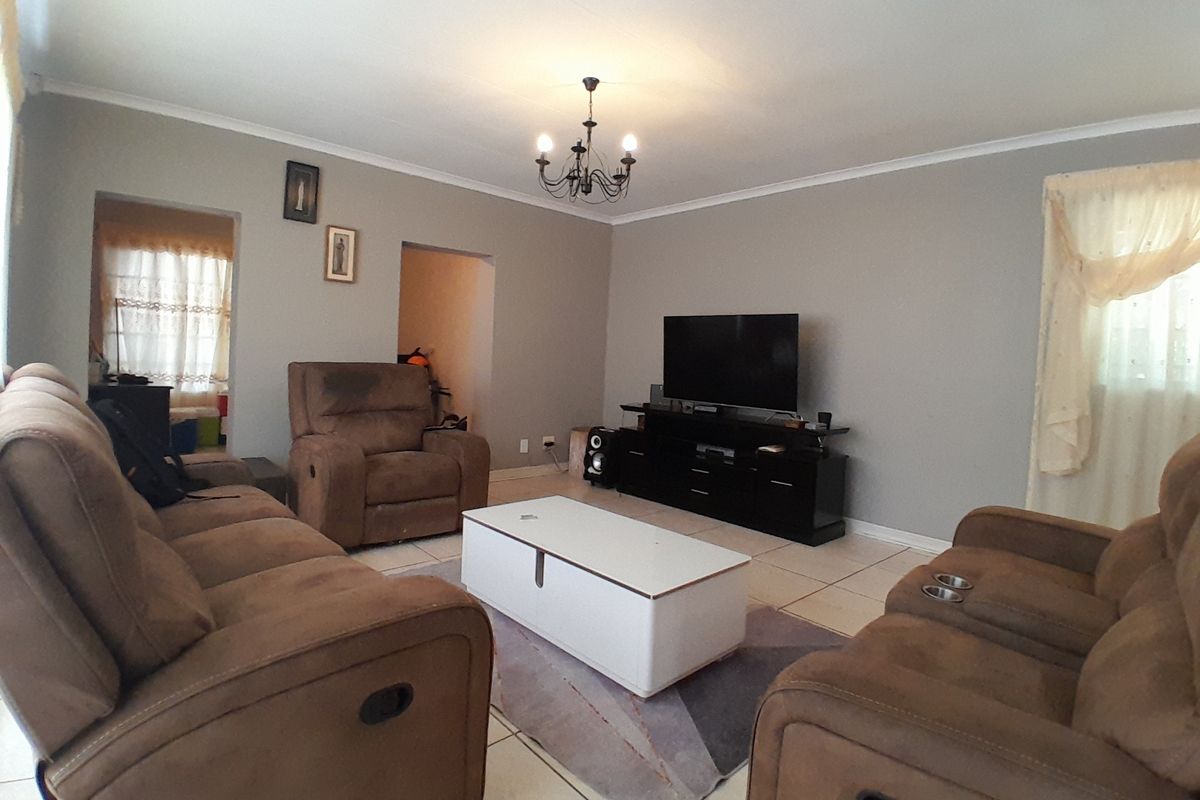 A spacious living room featuring neutral wall tones, tiled flooring, and a classic chandelier, providing a comfortable and functional family area.
