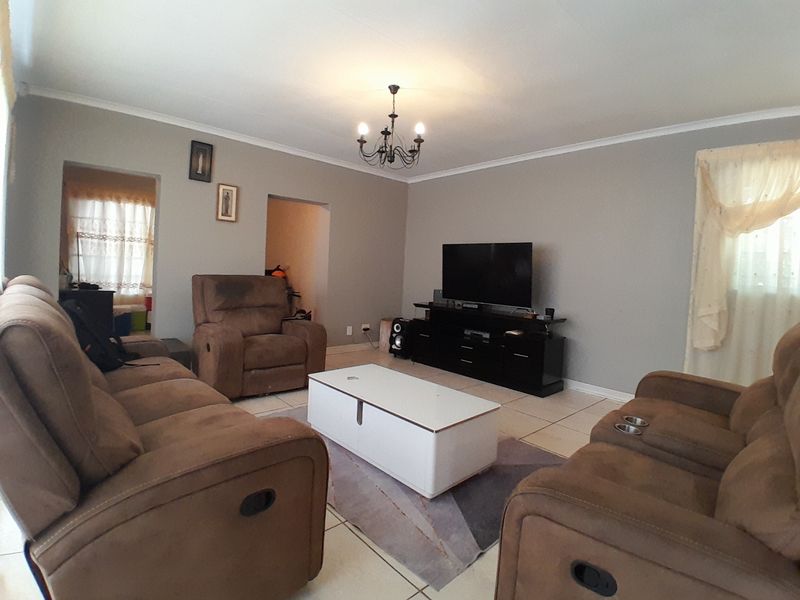 A spacious living room featuring neutral wall tones, tiled flooring, and a classic chandelier, providing a comfortable and functional family area.