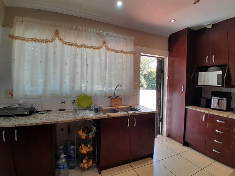 A functional kitchen featuring dark wood cabinetry, granite countertops, a double basin sink, and tiled flooring with direct access to the exterior.