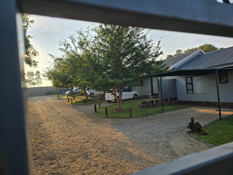 Front view of the property featuring a gravel driveway, carport, and well-maintained garden area.