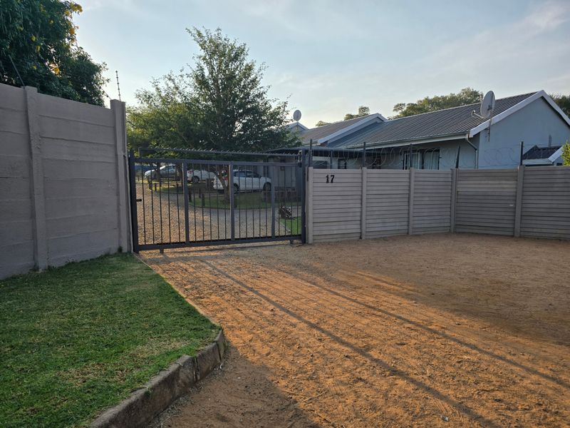 Front view of the property featuring a secure metal gate, precast concrete boundary wall with razor wire, and a metal roof house.