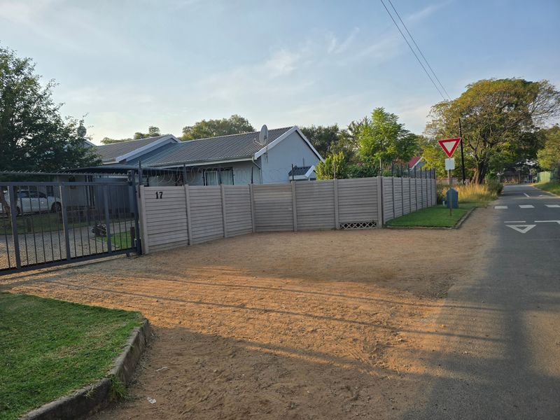 Front exterior view of the property featuring a metal sliding gate, precast boundary wall with security razor wire, and an unpaved driveway area.