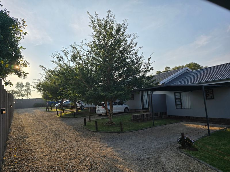Front exterior view of the property featuring a gravel driveway, carport, and well-maintained garden area.