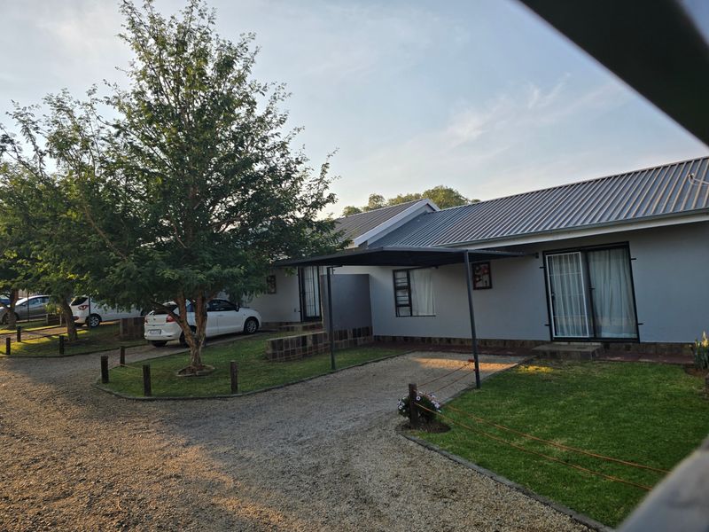 Front exterior view of a single-story house featuring a metal roof, a covered carport, and a well-maintained garden with a gravel driveway.