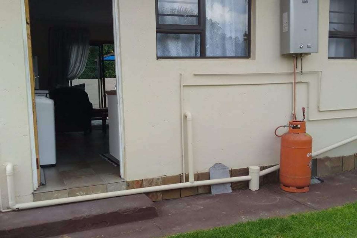 Rear exterior view of the property featuring a gas geyser installation, external plumbing, and access to the interior living space.