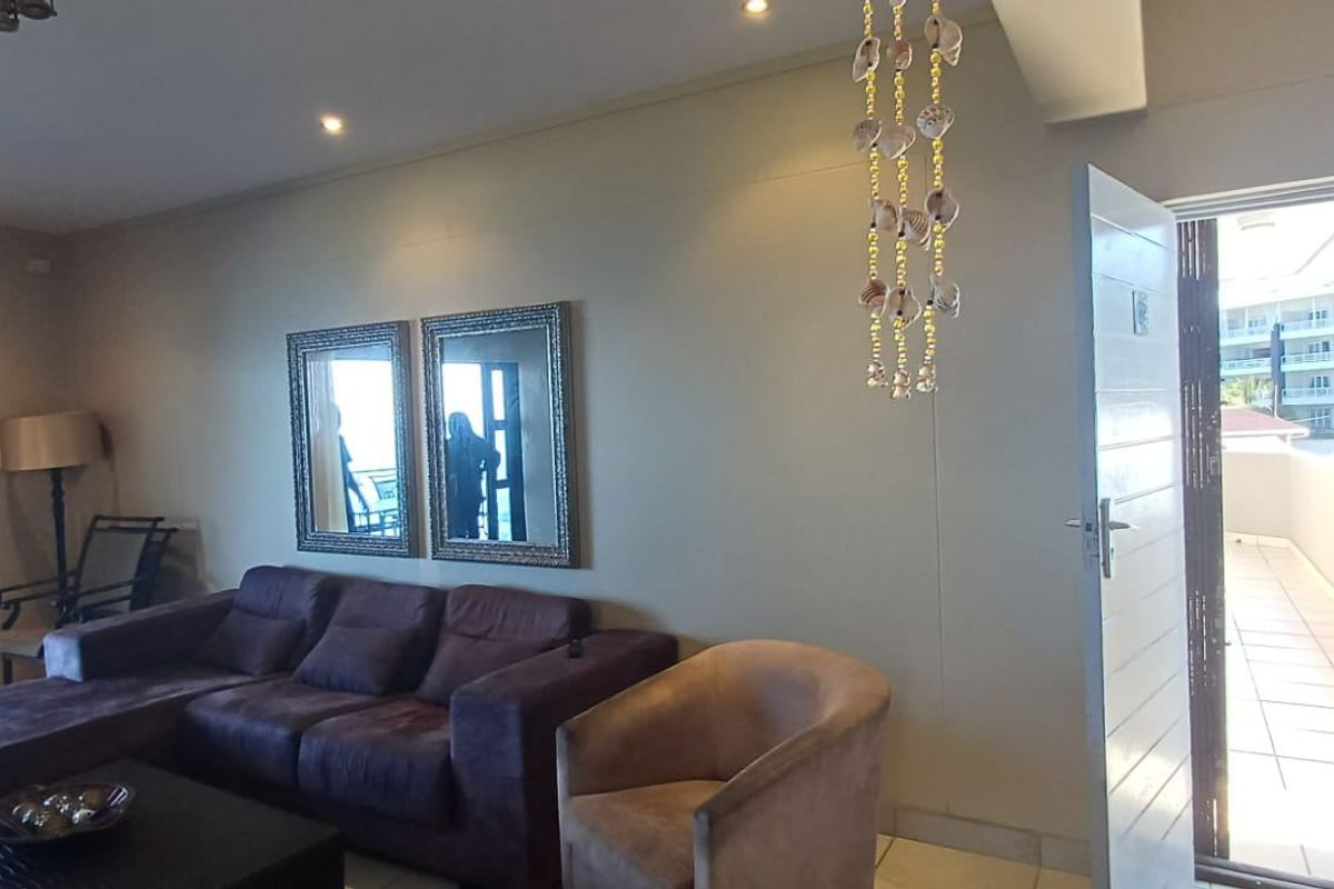 A spacious living area featuring tiled flooring, recessed ceiling lighting, and direct access to an outdoor balcony through a glass door.