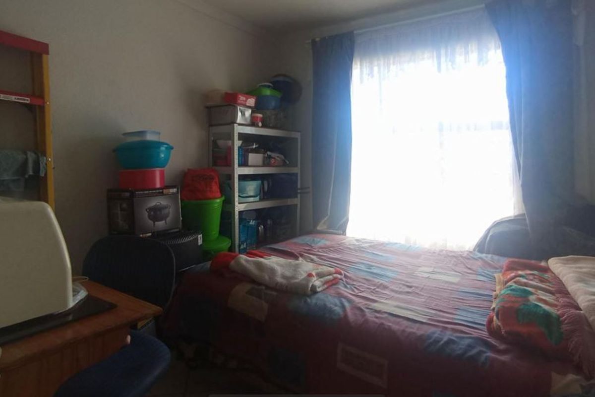 A bedroom featuring a window with curtains, providing natural light. The space is currently used for storage and sleeping.